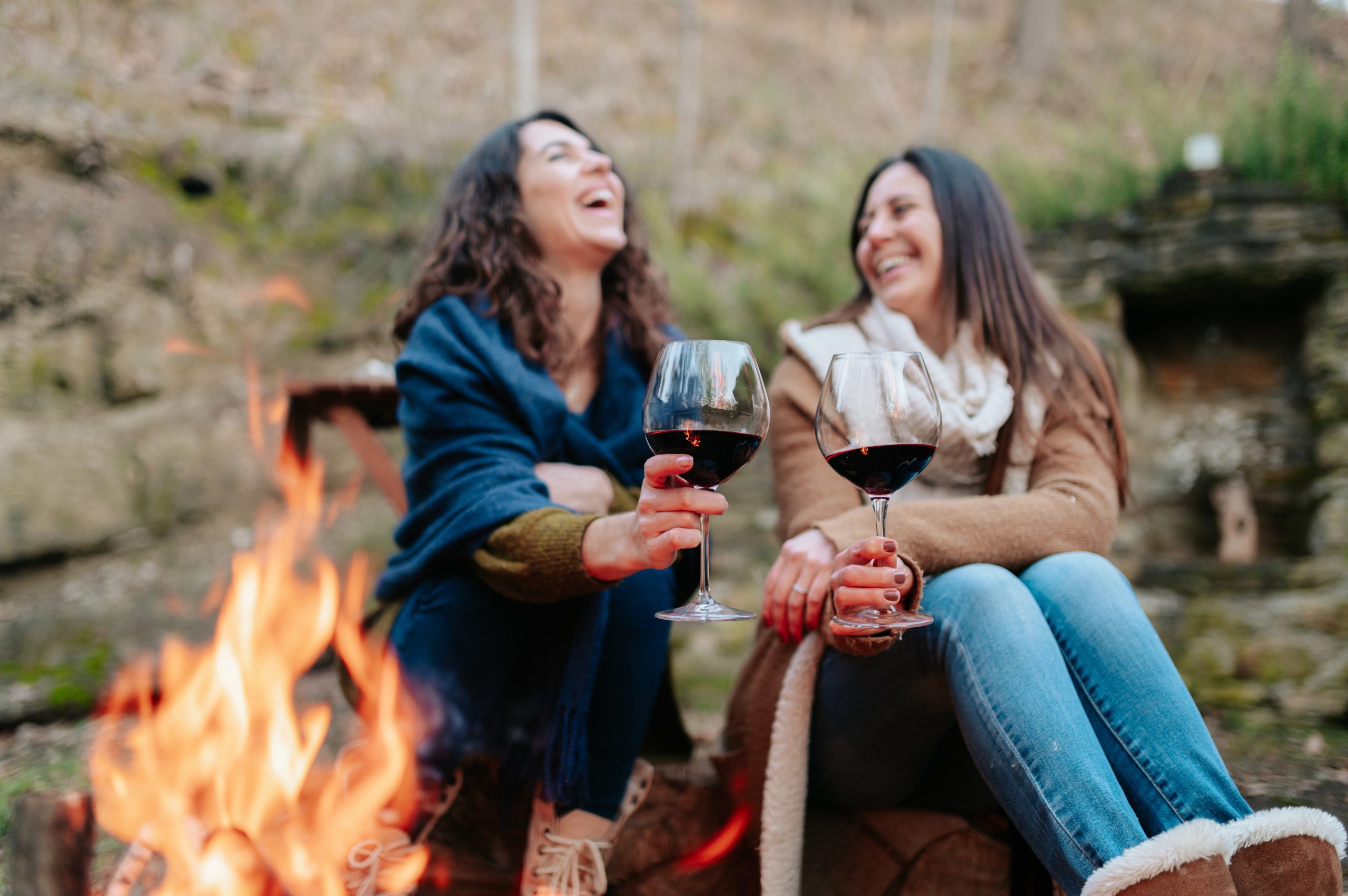 two friends talking and laughing drinking wine by fire